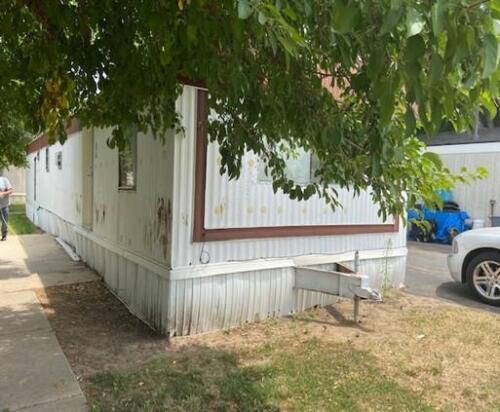 A white mobile home is parked next to a tree.